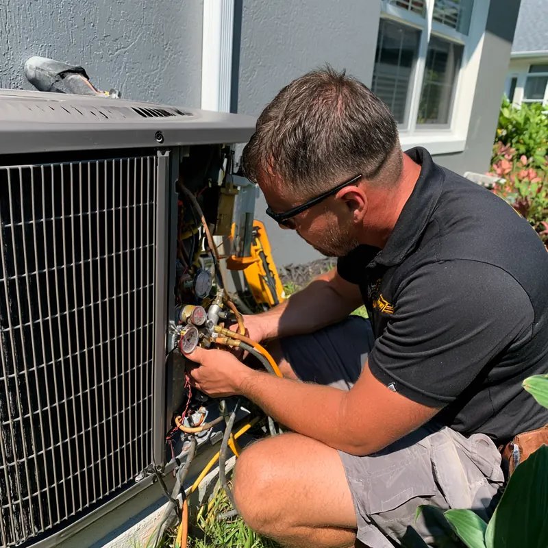HVAC technician in safety glasses reading manifold gauges connected to an outdoor air conditioner