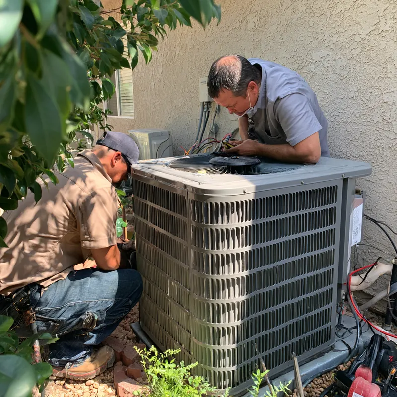 Two HVAC technicians working on an outdoor air conditioning condenser beside a house